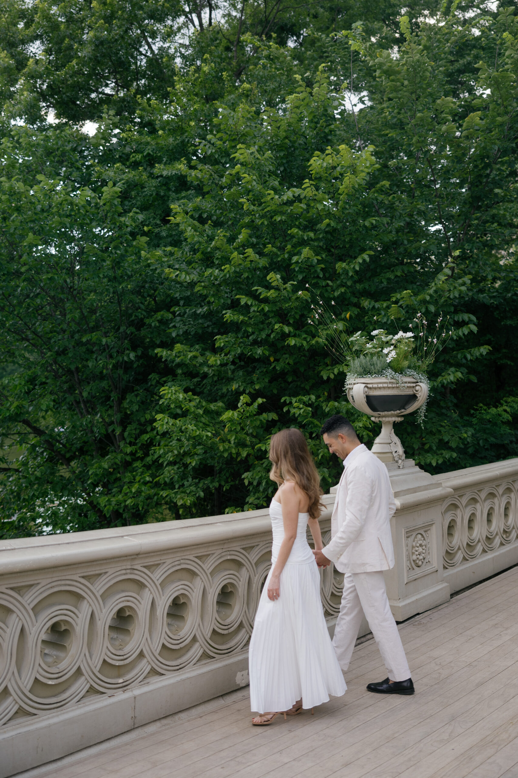 Couple walking hand-in-hand on Bow Bridge during their Central Park engagement session in New York City